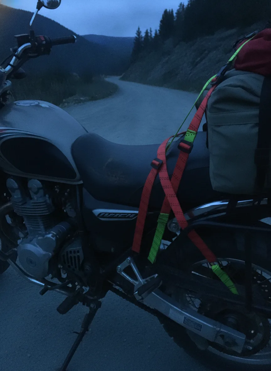 Close-up detail of elastic cargo straps securing motorcycle gear during blue hour mountain lighting.
