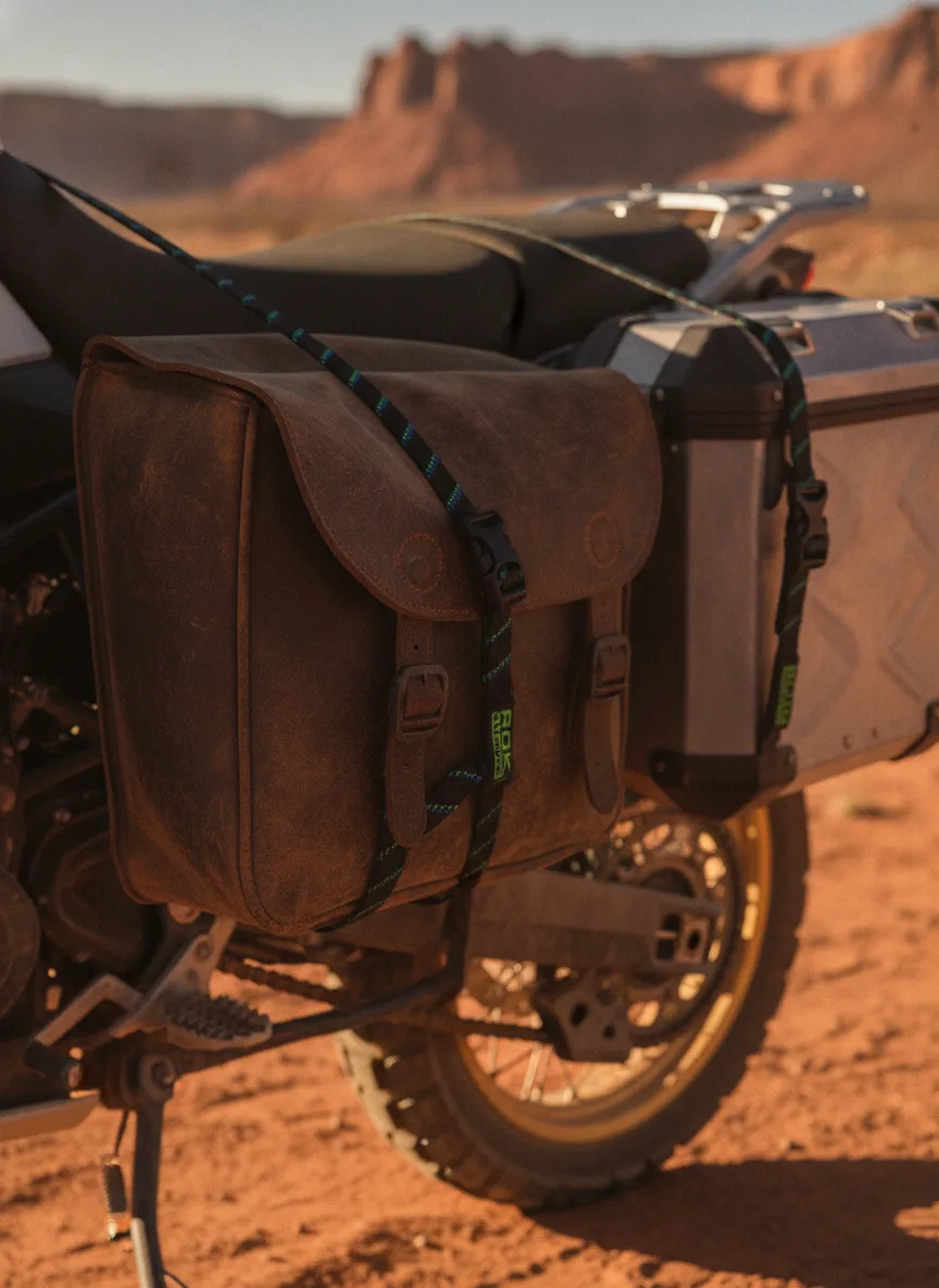 Elastic cargo straps with black buckles securing saddlebags to an adventure motorcycle in a desert landscape.